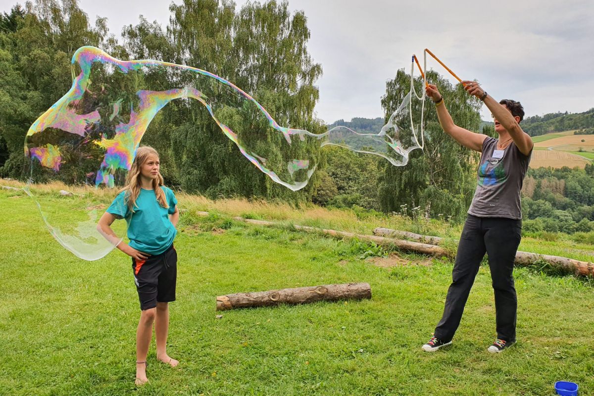 Zweo Personen spielen auf Wiese mit großen Seifenblasen, Gefühl von Spaß, Natur